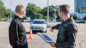 É possível rastrear a minha CNH pelo CPF? descubra agora! Instrutor e aluno diante de um carro em exame de direção, ilustrando como rastrear a CNH pelo CPF