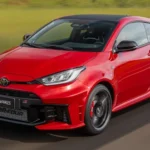 Toyota GR Yaris 2026 vermelho em movimento, vista frontal 3/4 em pista com teto preto