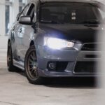 Mitsubishi Lancer sedã cinza vista frontal com faróis acesos