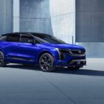 Cadillac Optiq AWD 2026 azul-metálico, vista frontal 3/4 em estúdio, com assinatura luminosa da grade e rodas grandes