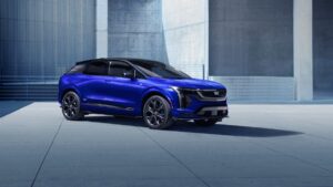 Cadillac Optiq AWD 2026 azul-metálico, vista frontal 3/4 em estúdio, com assinatura luminosa da grade e rodas grandes