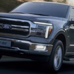 Ford F-150 branca rebocando trailer em vista traseira 3/4, destacando o engate e as luzes do reboque