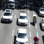 motociclista circulando entre faixas em avenida urbana, com carros lentos e trânsito intenso, vista de cima