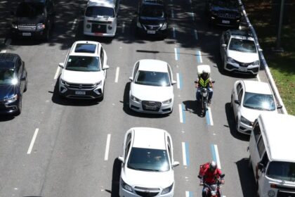 motociclista circulando entre faixas em avenida urbana, com carros lentos e trânsito intenso, vista de cima