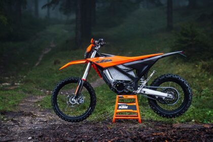 KTM Freeride E 2027 laranja, vista frontal 3/4 em trilha de terra com suspensão elevada e rodas 21/18