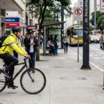 ciclista circulando corretamente na pista urbana, no mesmo sentido dos carros, com ciclovia ausente ao lado