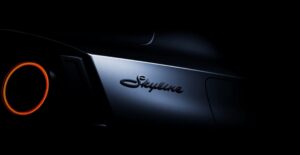 Novo Nissan Skyline em imagem teaser oficial, vista frontal em estúdio escuro, destaque para a grade e faróis com inspiração no R34, landscape