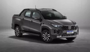 Fiat Strada 2026 branca, vista frontal 3/4 em rua urbana, com foco na grade e nos faróis