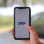 Documento digital da CNH no celular ao lado de carteira física, em mesa de atendimento de Detran
