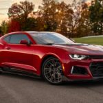 Chevrolet Camaro em vista frontal 3/4, cupê esportivo preto com rodas escurecidas e faróis acesos