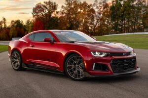 Chevrolet Camaro em vista frontal 3/4, cupê esportivo preto com rodas escurecidas e faróis acesos