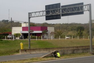 Radar fixo visível em avenida urbana brasileira com placa de limite de velocidade e painel eletrônico, foto horizontal