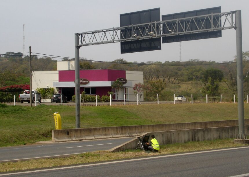 Radar fixo visível em avenida urbana brasileira com placa de limite de velocidade e painel eletrônico, foto horizontal