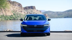 Nissan Sentra: A renovação muda a briga com Corolla? Nissan Sentra 2026 prata, vista frontal 3/4 em ambiente urbano, destaque para faróis de LED e grade dianteira