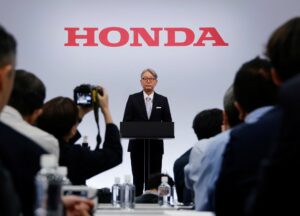 Honda recua nos elétricos e segura aposta nos híbridos Apresentação de resultados da Honda com gráfico de eletrificação e executivo no palco, foto horizontal de coletiva corporativa