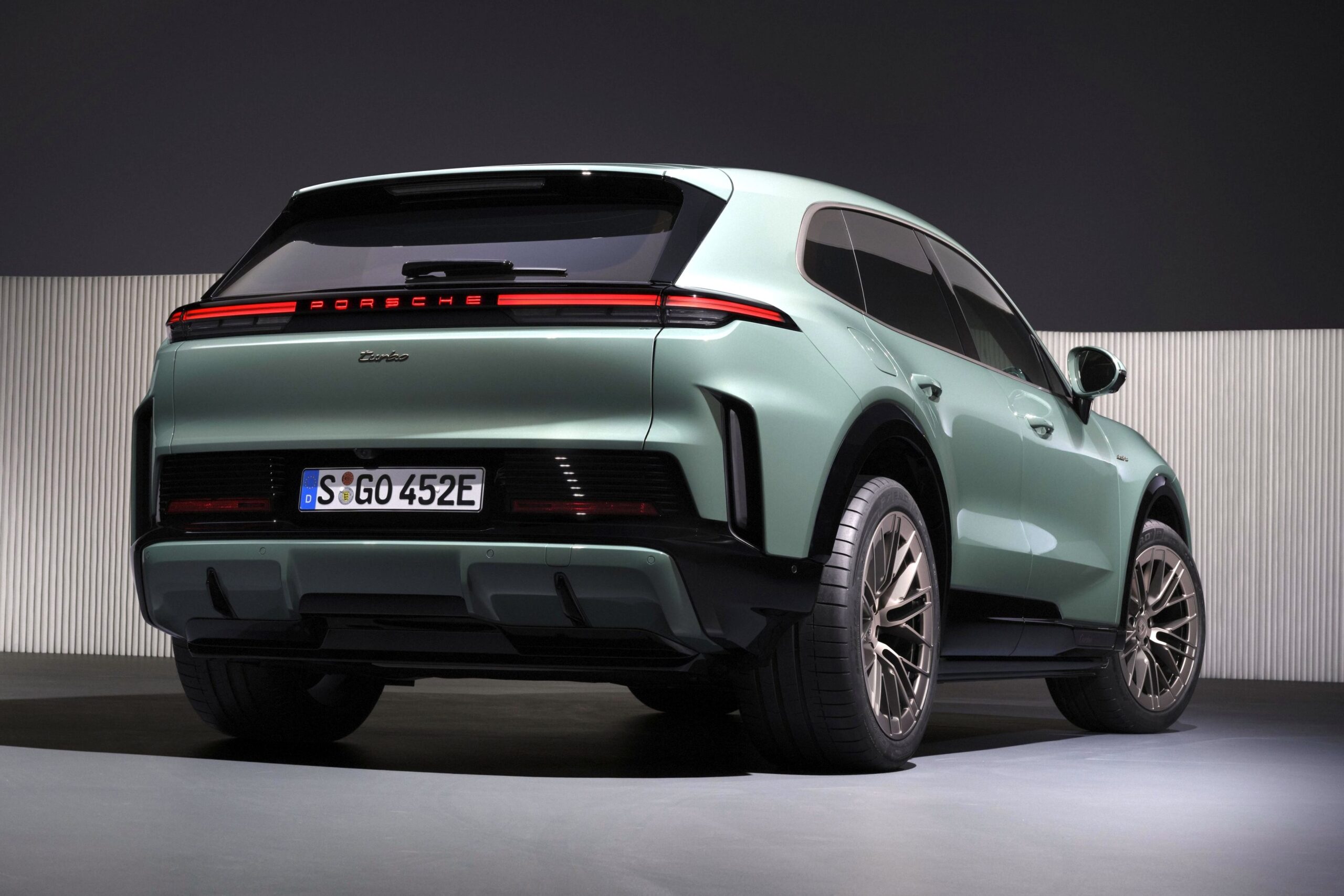 SUV Porsche Cayenne Turbo E-Hybrid verde-claro, visto de traseira e lateral, com lanternas conectadas e placa alemã S GO 452E, em ambiente escuro com parede listrada