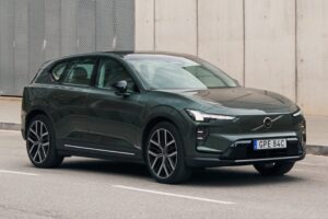 Volvo EX60 com Gemini não livra multa pelo CTB SUV elétrico Volvo EX30 verde escuro, visto de frente e lateral, parado em uma rua asfaltada com faixas brancas, em frente a uma parede cinza texturizada