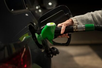 Frentista abastecendo carro flex em posto brasileiro, detalhe da bomba de gasolina comum com visor de preço, foto horizontal
