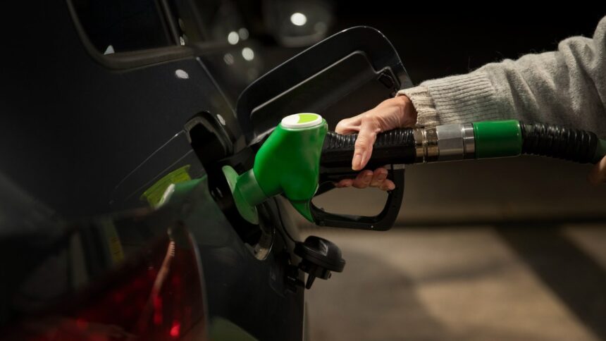Frentista abastecendo carro flex em posto brasileiro, detalhe da bomba de gasolina comum com visor de preço, foto horizontal