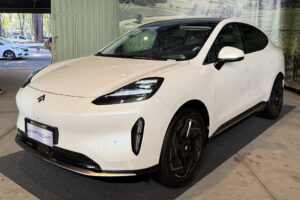 GAC Hyptec HT 2027 em foto frontal três quartos, cor escura, parado em avenida urbana, landscape