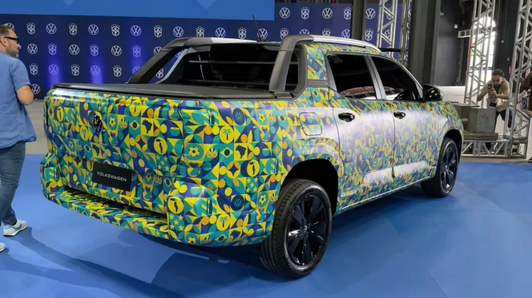 Camuflada, Volkswagen Tukan 2027 já revela foco em carga Volkswagen Tukan camuflada em vista lateral rodando em estrada, com caçamba fechada e cabine dupla, horizontal