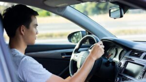 Atenção: Mão solta no volante pode gerar multa Motorista de carro de passeio com uma mão no volante e outra acionando a alavanca de câmbio manual, foto interna horizontal