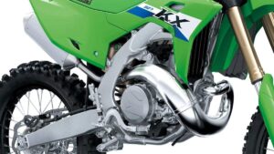 Kawasaki KX de competição em foto frontal horizontal numa pista de motocross, visual verde da marca e salto de terra ao fundo