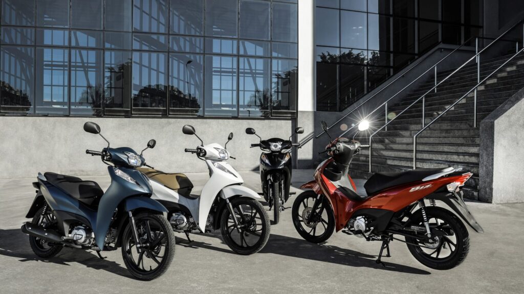 Honda Biz 125: por que ela nunca sai de linha Linha completa da Honda Biz 125 estacionada mostrando as versões em diferentes cores disponíveis