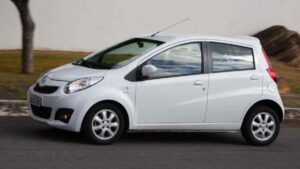 JAC Motors: 85 elétricos e rede menor no Brasil Concessionária JAC Motors brasileira com fachada parcialmente fechada e poucos veículos no pátio, fotografia horizontal, luz natural