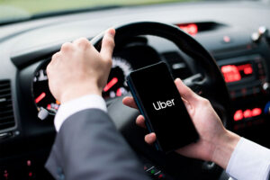 Uber testa taxa de até R$ 1,88 por corrida recusada motorista da Uber olhando uma solicitação de corrida no celular dentro do carro, painel visível e enquadramento horizontal landscape
