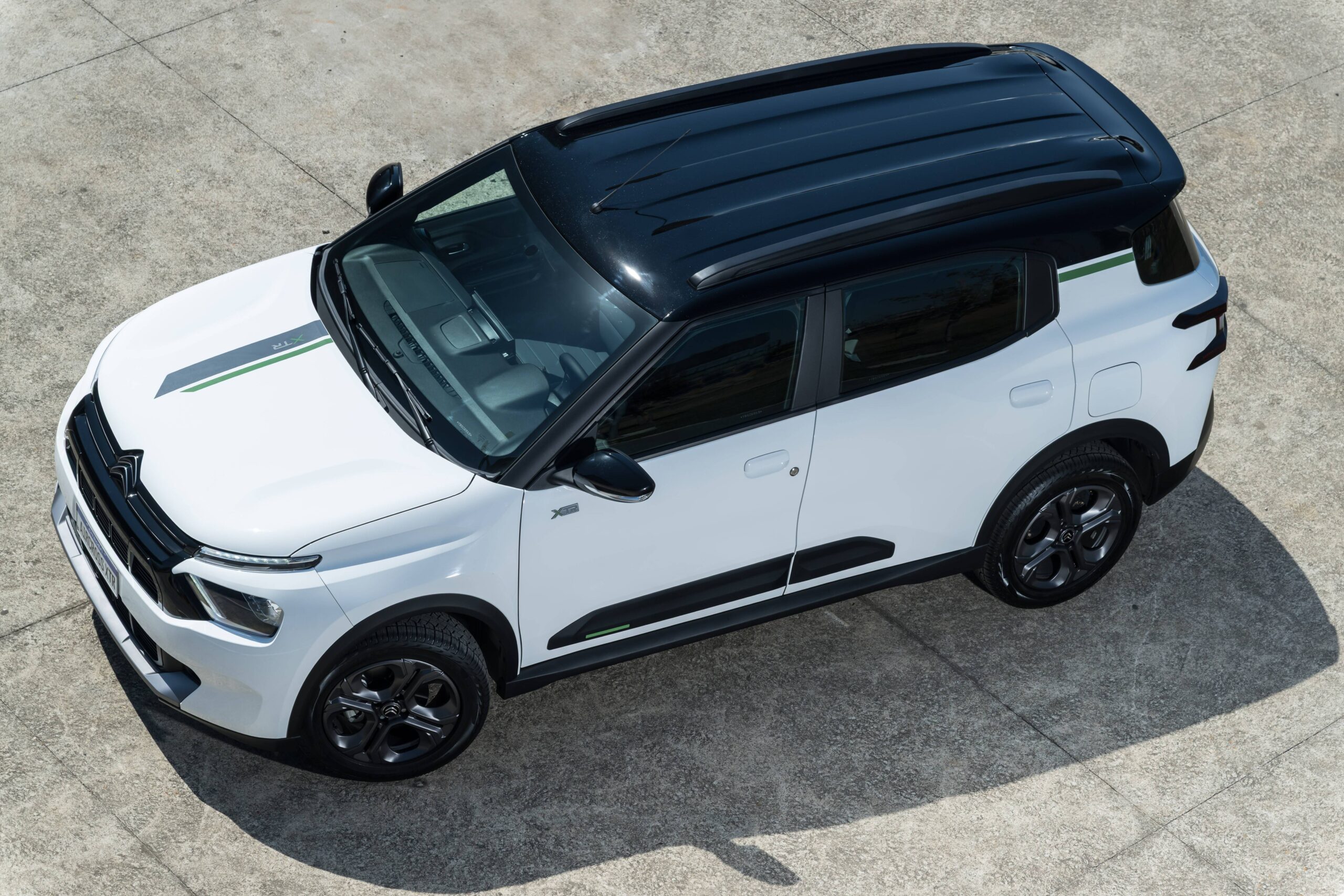 SUV Citroën C3 Aircross branco com teto preto, faixas decorativas cinza e verde no capô e na lateral, rodas escuras, estacionado em piso de concreto cinza, visto de cima