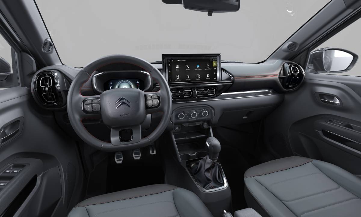 Citroën Basalt 2027: Preços partem de R$ 95.590 Interior de um carro moderno com painel cinza escuro, volante multifuncional, tela multimídia central com ícones de aplicativos e câmbio manual. Detalhes em laranja no painel e bancos de tecido cinza escuro e claro.
