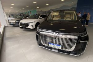 Voyah no Brasil: Quatro modelos e até 1.530 km Logotipo Voyah em uma apresentação automotiva, com um carro de luxo da marca ao fundo, fotografia horizontal landscape