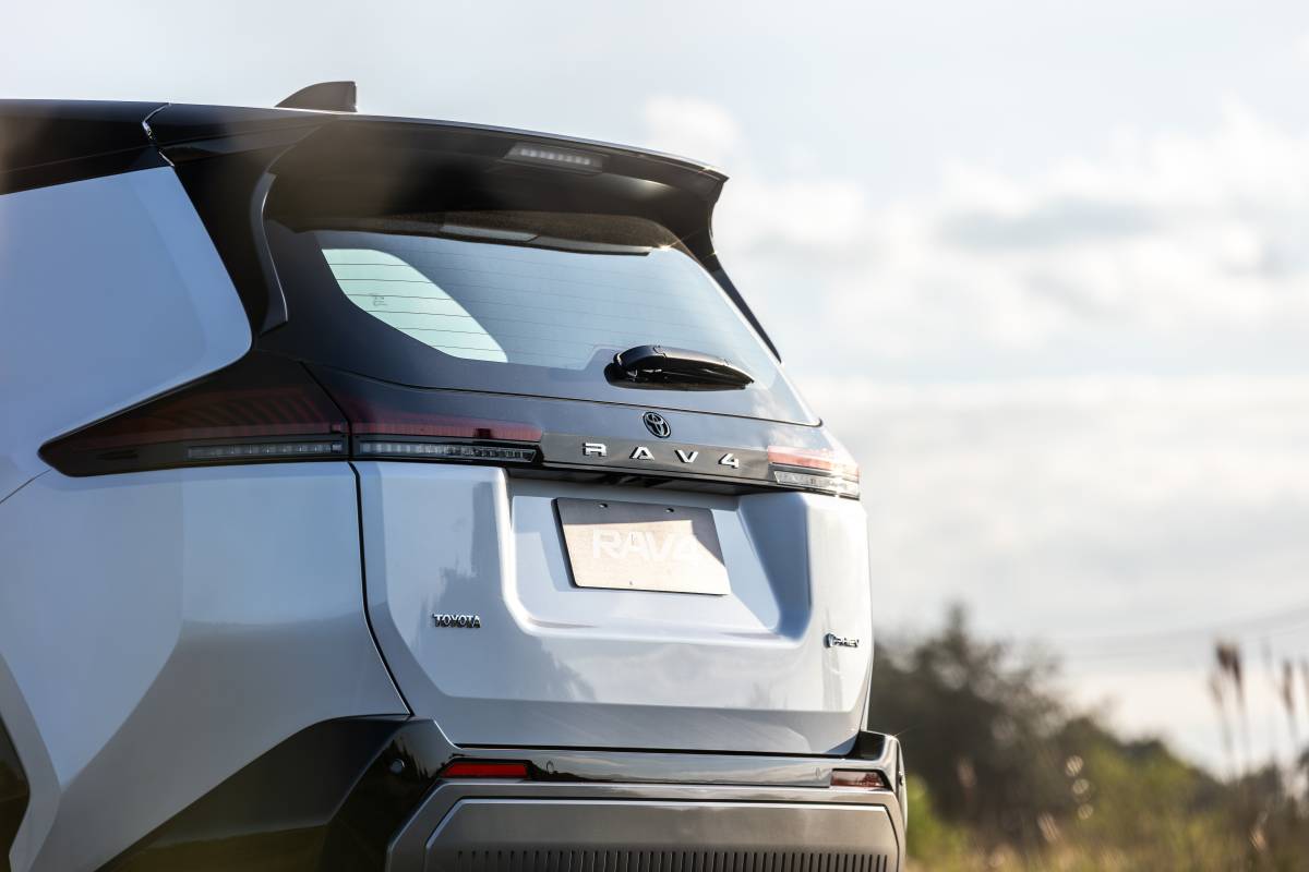 Toyota RAV4 PHEV: R$ 399.990 contra BYD Atto 8 Traseira de um SUV Toyota RAV4 cinza claro, com lanternas horizontais escuras e aerofólio preto, sob céu azul com nuvens esparsas