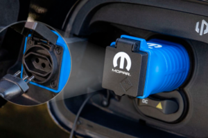 Adaptador Mopar de alimentação externa conectado a um carro elétrico Leapmotor, com tomada e equipamentos de camping ao lado, orientação horizontal
