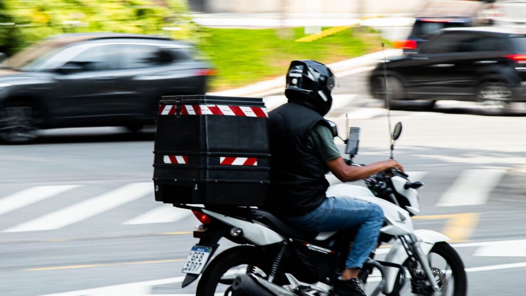 Motoboy com baú de entrega em avenida brasileira, motofrete exige EAR na CNH